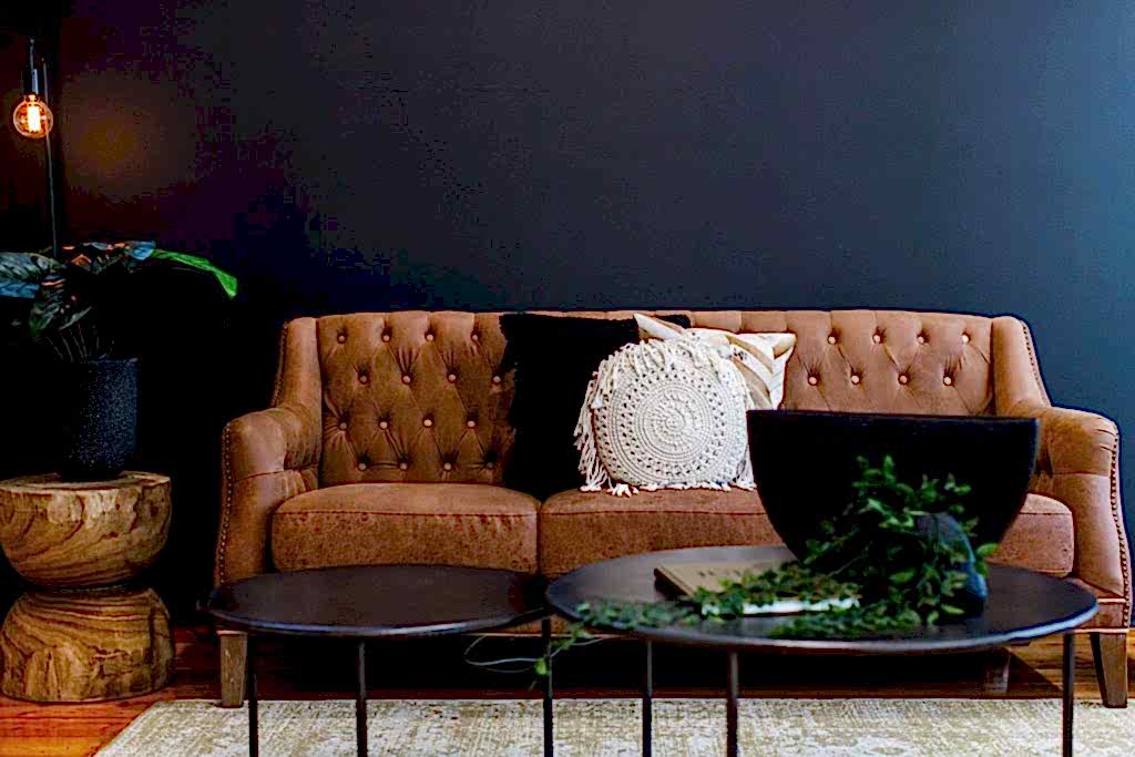 Two round coffee tables in front of brown leather lounge with brown and white pillows